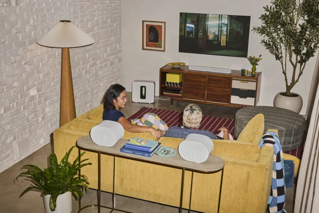 Woonkamer met een witte Sonos Beam Ultra onder de tv, een Sub Mini en twee Era 100's achter de bank