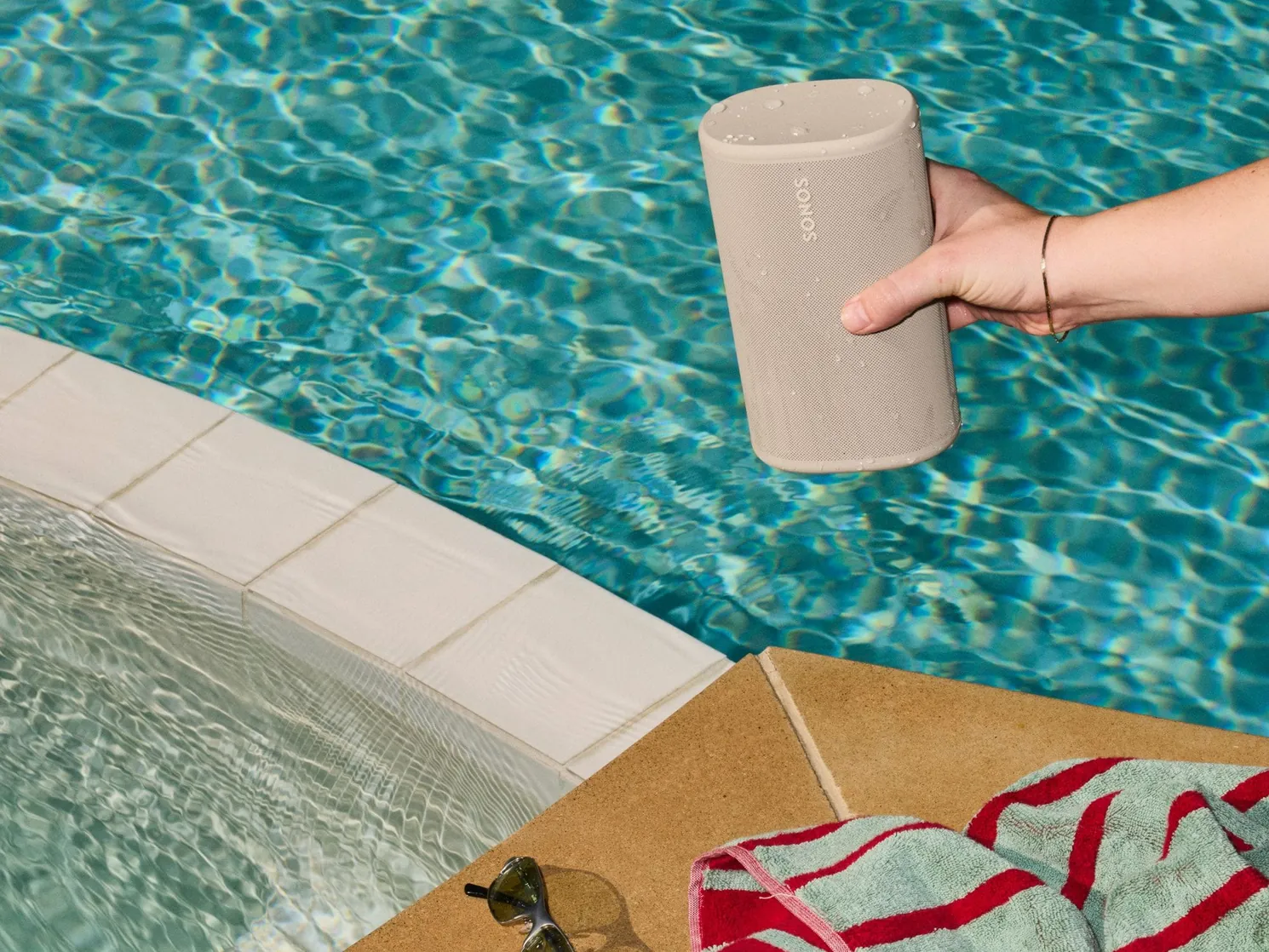 Hand die een natte Sonos Play in de kleur sand boven een zwembad houdt